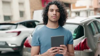 Young latin man smiling confident using touchpad at street