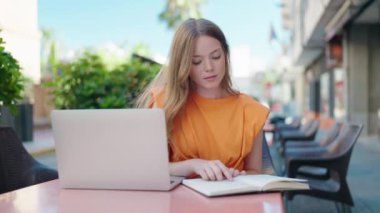 Genç bir kadın kahve dükkanının terasında ders çalışıyor.