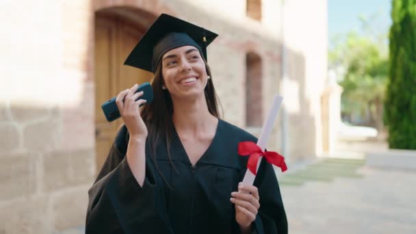 Young Hispanic Woman Wearing Graduated Uniform Holding Diploma Hearing Audio — Stockvideo