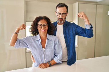 Middle age couple standing together strong person showing arm muscle, confident and proud of power 