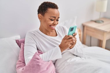 Afrika kökenli Amerikalı bir kadın yatak odasında akıllı telefon kullanıyor.