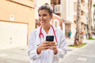 Sokakta akıllı telefon kullanan doktor üniforması giyen genç sarışın kadın.