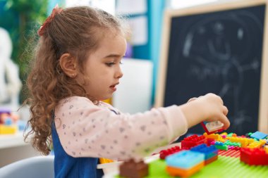 Adorable blonde girl playing with construction blocks sitting on table at kindergarten