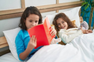 Two kids reading story book sitting on bed at bedroom