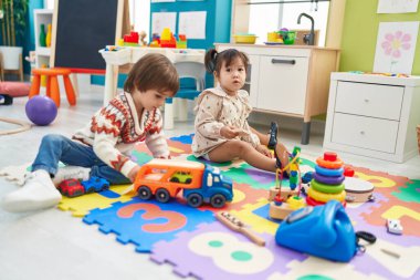 Two kids playing with cars toy sitting on floor at kindergarten