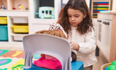 Adorable hispanic girl playing with doll at kindergarten