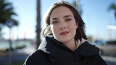 Young blonde woman standing with serious expression at park