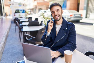 Genç İspanyol adam akıllı telefondan konuşuyor. Kahve dükkanının terasında dizüstü bilgisayar kullanıyor.
