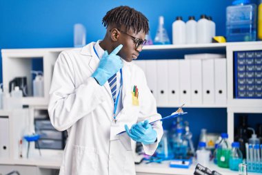 African american man scientist reading report with doubt expression at laboratory