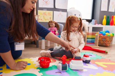 Teacher and student playing supermarket game sitting on floor at kindergarten