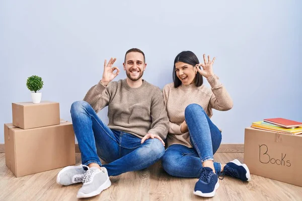 stock image Young couple moving to a new home smiling positive doing ok sign with hand and fingers. successful expression. 