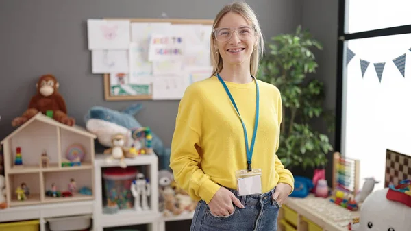 Young blonde woman working as teacher smiling happy at kindergarten