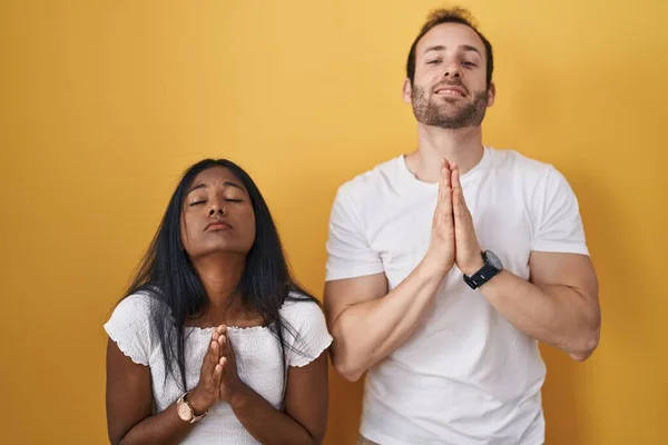 Międzyrasowa Para Stojąca Nad Żółtym Tłem Żebrząca Modląca Się Rękami — Zdjęcie stockowe
