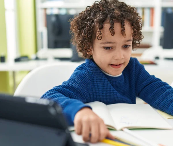Adorable hispanic boy preschool student sitting on table drawing on notebook at classroom