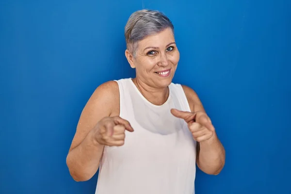 中年の白人女性が青の背景に立って カメラに幸せと面白い顔を指を指している 良いエネルギーと振動は — ストック写真