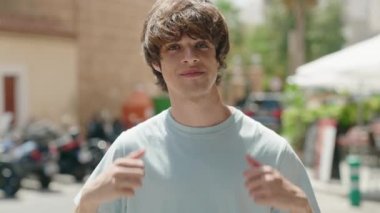 Young blond man smiling confident doing ok sign with thumbs up at street