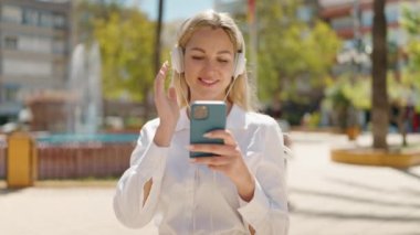 Young blonde woman listening to music at park