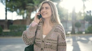 Genç sarışın kadın gülümsüyor. Kendine güveni tam. Akıllı telefondan konuşuyor.