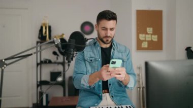 Genç İspanyol sanatçı, müzik stüdyosunda akıllı telefon kullanarak gülümsüyor.