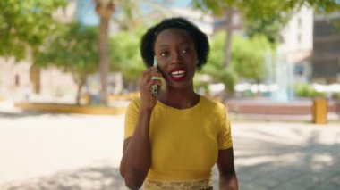 Afro-Amerikalı kadın gülümsüyor. Parktaki akıllı telefondan konuşuyor.