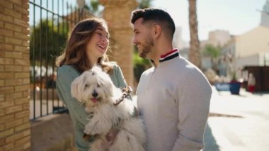 Young couple smiling confident holding dog at street