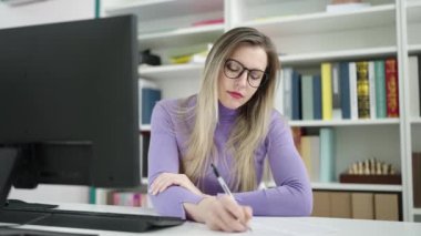 Kütüphane üniversitesinde doküman üzerine bilgisayar kullanan genç sarışın kız öğrenci.