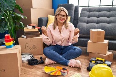 Young hispanic woman moving to a new home sitting on the floor excited for success with arms raised and eyes closed celebrating victory smiling. winner concept. 