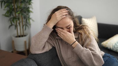 Young beautiful hispanic woman sitting on sofa crying at home