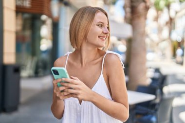 Sokakta akıllı telefon kullanan, kendine güvenen genç sarışın kadın.