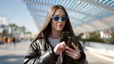 Parkta akıllı telefon kullanarak gülümseyen güzel bir İspanyol kadın.