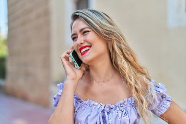 Genç, güzel, İspanyol bir kadın gülümsüyor ve caddede akıllı telefondan konuşuyor.