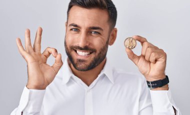 Yakışıklı İspanyol adam litekoin kripto para tutuyor. Parmaklarıyla imza atıyor, gülümsüyor. Mükemmel bir sembol. 