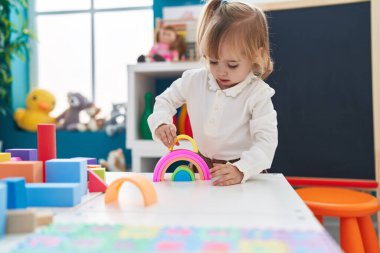 Adorable blonde girl playing with toys standing at kindergarten