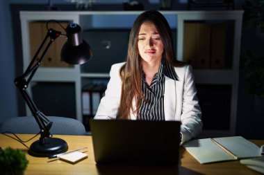 Young brunette woman working at the office at night with laptop depressed and worry for distress, crying angry and afraid. sad expression. 