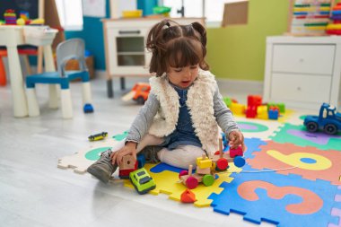 Adorable hispanic toddler playing with car toy sitting on floor at kindergarten
