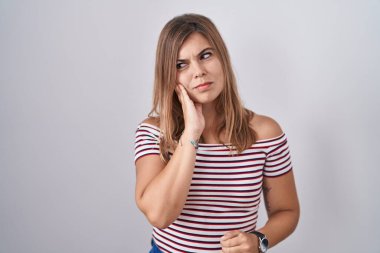 Tecrit edilmiş arka planda duran genç İspanyol kadın diş ağrısı ya da diş hastalığından dolayı acı dolu bir ifadeyle ağıza dokunuyor. dişçi 