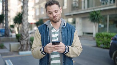 Young caucasian man smiling using smartphone at street