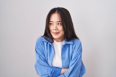 Young chinese woman standing over white background shaking and freezing for winter cold with sad and shock expression on face 