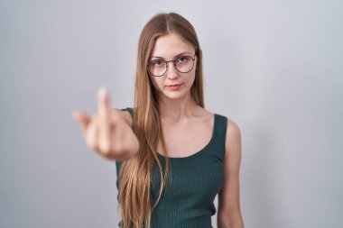 Young caucasian woman standing over white background showing middle finger, impolite and rude fuck off expression 