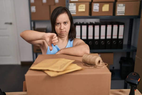 stock image Hispanic girl with down syndrome working at small business ecommerce with angry face, negative sign showing dislike with thumbs down, rejection concept 