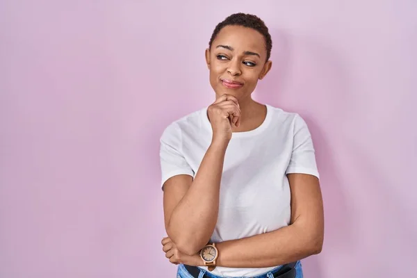 Beautiful african american woman standing over pink background with hand on chin thinking about question, pensive expression. smiling and thoughtful face. doubt concept.