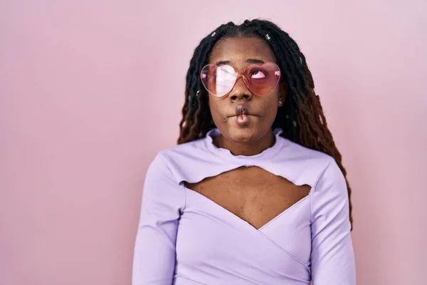 stock image African woman with braided hair standing over pink background making fish face with lips, crazy and comical gesture. funny expression. 