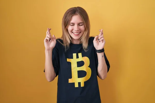 Blonde Caucasian Woman Wearing Bitcoin Shirt Gesturing Finger Crossed Smiling — Stok fotoğraf