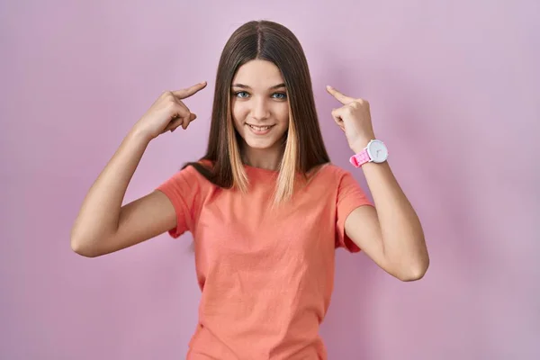 Teenager Dívka Stojící Nad Růžovým Pozadím Úsměvem Ukazuje Hlavu Oběma — Stock fotografie