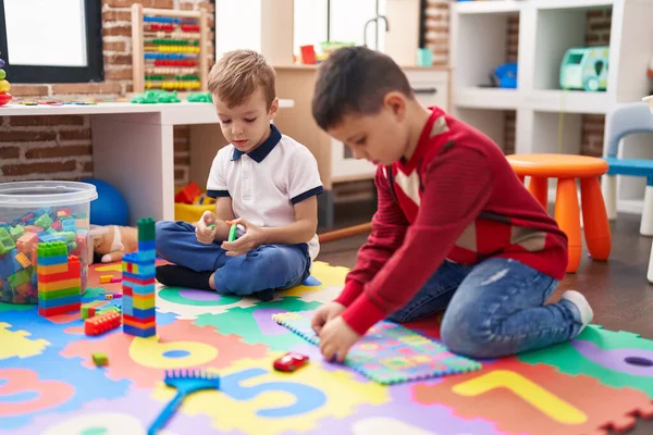 建設ブロックと数学のパズルゲームで遊んでいる2人の子供が幼稚園で床に座っている — ストック写真