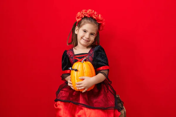 stock image Adorable hispanic girl wearing halloween costume holding pumpkin over isolated red background