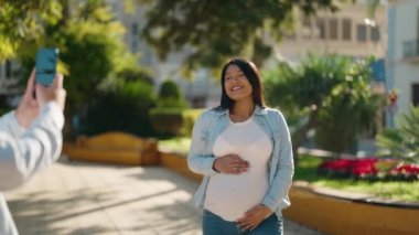 Genç Latin çift gülümsüyor. Parktaki akıllı telefonun yanında fotoğraf çekiyorlar.