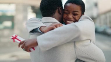 African american couple hugging each other surprise with anniversary gift at street