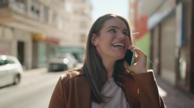 Beyaz bir kadın gülümsüyor ve caddede akıllı telefondan konuşuyor.