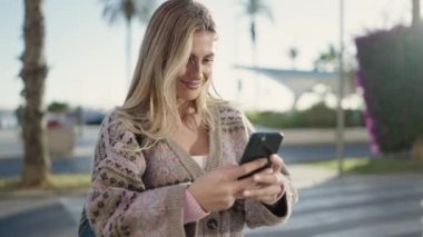 Sokakta akıllı telefon kullanan, kendine güvenen genç sarışın kadın.